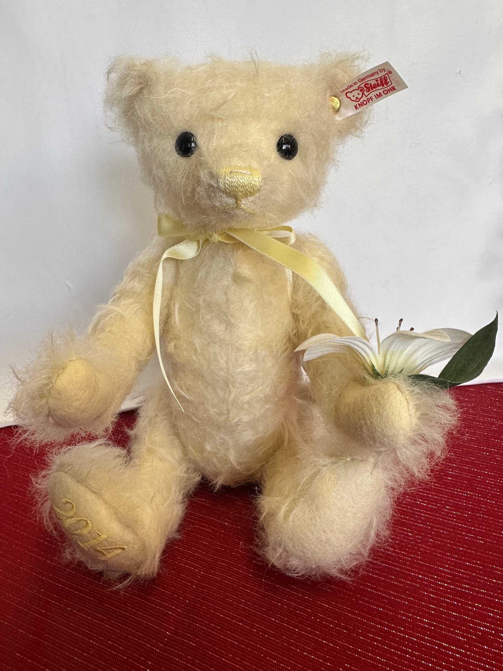 Steiff Teddy Bear holding a lily blossom wearing a yellow ribbon